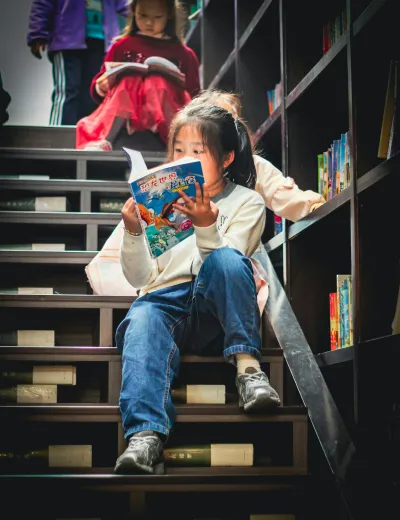 Child reading a picture book on a library staircase